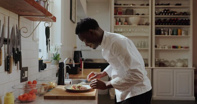 Black man, chef and plating food in kitchen for presentation, culinary skills and herbs for flavor. Male person, cooking and garnish steak of lunch service, meat process and prepare cuisine at house - Powered by Adobe