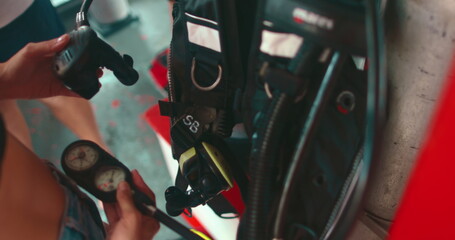 Diver is preparing scuba diving equipment and checking the oxygen gauge before a dive in thailand. The diver is wearing a black wetsuit and holding a black scuba tank