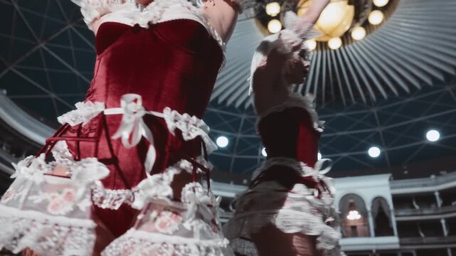 Two beautiful showgirls with white hair are sensually dancing on stage in an empty theater. They're wearing red velvet and white lace lingerie costumes.