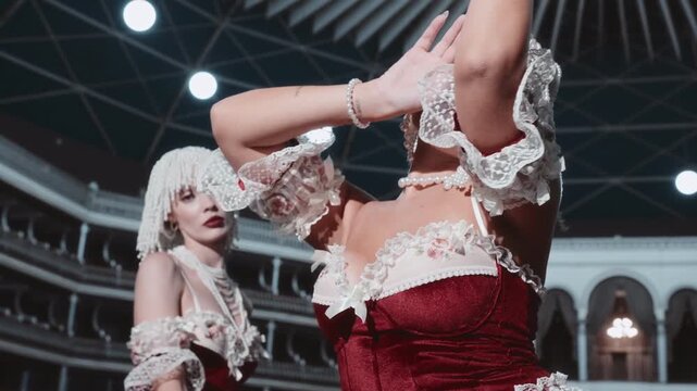 Two women in red burlesque lingerie and pearl headdresses pose sensually on a theater stage.