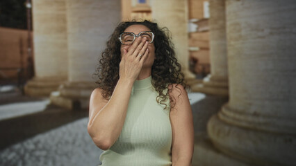 Woman wearing eyeglasses in a sleeveless top clapping hands on a cobbled street near a historic...