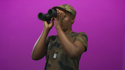 Fototapeta premium Woman in camouflage uniform holds binoculars to her eyes in a studio setting on a purple backdrop; vigilance watching exploration.
