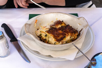 Traditional baked lasagna served in a ceramic dish on a white plate at an outdoor restaurant