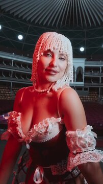 A beautiful young woman in a vintage-style lingerie poses and dances in an empty theater with dramatic red lighting.