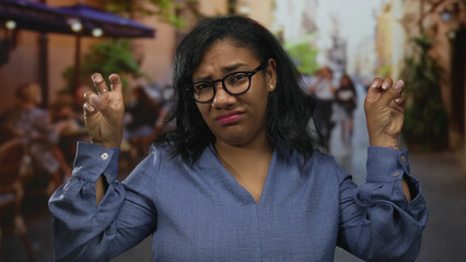 Woman wearing glasses and a blue blouse making finger quotes gesture and rolling eyes on street;...