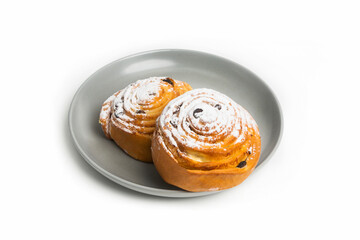 Two sweet buns with raisins and cinnamon sprinkled with powdered sugar lie on a gray plate. Isolated