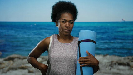 Woman standing on a beach holding a yoga mat against a serene seaside backdrop, portraying tranquility and fitness