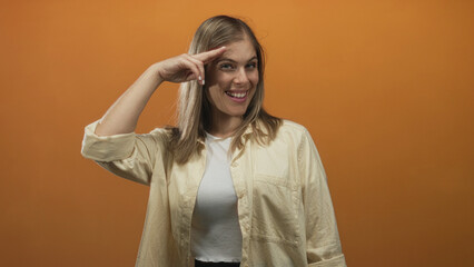 Smiling woman pointing finger upward on orange studio backdrop; confidence optimism positivity...
