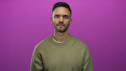 Young hispanic man in sweater gestures with intensity against bright pink background conveying...