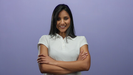 Obraz premium Woman smiling with arms crossed, wearing white shirt, standing against a purple background, exuding confidence and happiness in an isolated studio setting.