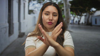 Fototapeta premium Woman stands with hands on hips on sunlit narrow city street lined with white walls; confidence independence.