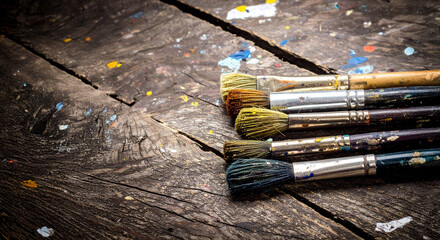 Paintbrushes resting on a colorful wooden table are showing signs of extensive use