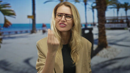 Woman gesturing passionately on a sunny promenade by the beach, with a backdrop of palm trees and blue sea, exuding strong emotions in an outdoor candid scene.