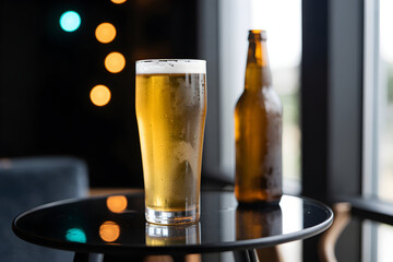 Refreshing pint of golden beer and a frosty bottle on a dark table with soft bokeh lights