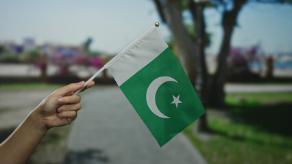Hand of man holding pakistan flag outdoors in a city street setting, capturing a moment of national...