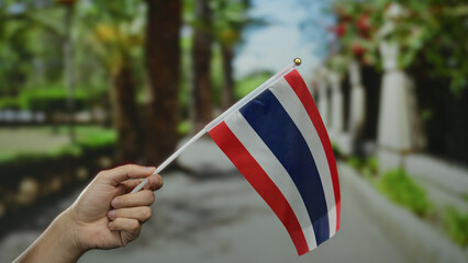 Hand of a person holding thai flag on a sunny street in thailand, showcasing patriotism in a vibrant outdoor urban setting.