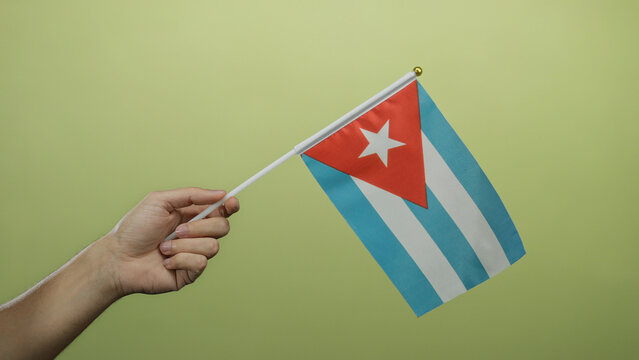 Caucasian man holding cuban flag against a yellow background wall showcasing national pride and cultural emblem.