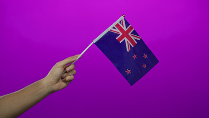 Man holding new zealand flag against pink background, showcasing national pride and identity with a clear isolated view of the flag and hand.