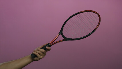 Man holding tennis racket against pink wall showing isolated hand and sports equipment in a...