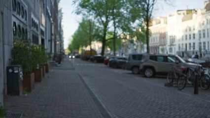 European city street scene with blurred focus showcasing parked cars, bicycles, and cobblestone pavement in a serene residential neighborhood under clear skies.