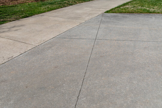 Narrow concrete path feeding into a wider concrete area, green grass and creative copy space, horizontal aspect