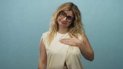 Woman touching chest with right hand and raising left hand while wearing cream top in light blue...