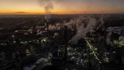 Vista aérea de uma indústria de papel e celulose com chaminés e galpões em funcionamento, cercada por áreas verdes