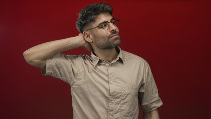 Obraz premium Hispanic man touching neck with hand against red studio wall, eyes closed and head tilted slightly in thoughtful posture; inner unease.