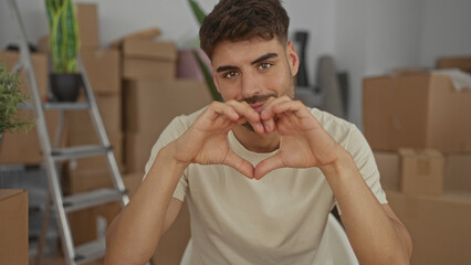 Man makes heart shape with hands in new home building surrounded by cardboard boxes and potted...