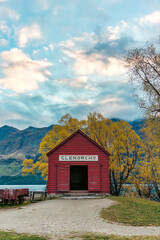 Famous Glenorchy red boat shed by Lake Wakatipu among golden autumn trees and mountian range in New Zealand