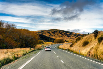 Scenic view of car driving on winding road through golden hill and wilderness during autumn season in New Zealand