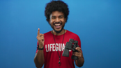 African american lifeguard man holding binoculars shows a gesture of having an idea against a vibrant blue background, embodying alertness and safety.