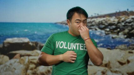 Young man at seaside wearing green shirt with volunteer text enjoying beach scenery in bright sunlight