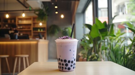 A light purple bubble tea drink with black tapioca pearls, garnished with purple flowers, sits on a light wooden table in a cafe.
