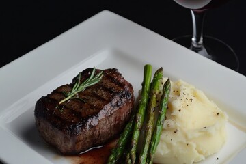 Grilled steak, asparagus, and creamy mashed potatoes served on a white plate, complemented by a glass of red wine.