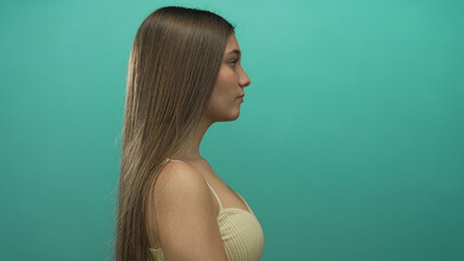 Teenage girl shows bare shoulder and hair in a posed side profile with teal studio backdrop; calm...