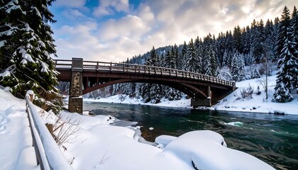 A scenic winter vista showcasing a bridge spanning a turquoise river. Snow blankets the banks and evergreen forest. Overcast sky with slivers of sun. Pathway on the left leads toward the bridge