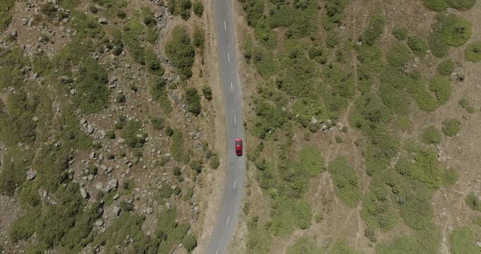 Aerial view of a lone red car traveling along a winding road, cutting through the rugged terrain of Mount Aragats, Shirak Province, Armenia.