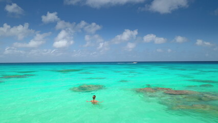 Woman swimming in crystal turquoise sea water under blue clouds sky in sunny day. Tourist girl relax and enjoy outdoor lifestyle travel on summer holiday vacation. Aerial view drone