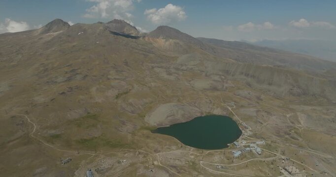 Aerial view of Mount Aragats' rugged slopes meeting the tranquil, dark waters of a lake, creating a stark contrast, Mount Aragats, Shirak Province, Armenia.