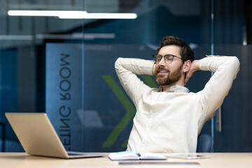 Satisfied with work and relaxed young male businessman sitting in the office at the desk with his eyes closed and resting