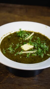 Delicious saag paneer served in a white bowl on a wooden table background
