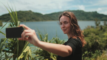 Woman makes selfie mobile photo enjoying tropical jungles and mountain lake landscape. Nature freedom adventure, happy vacation video call, girl tourist outdoors. Travel, tourism, holiday in Polynesia