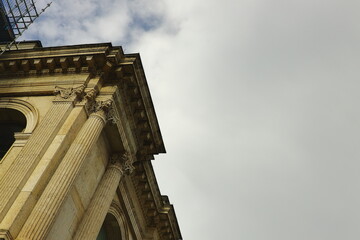 Historic building facade with classical columns and decorative details against cloudy sky, architectural minimalism concept.