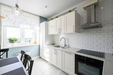 bright kitchen with white cabinets, a tile backsplash, and a window overlooking a cityscape. Black chairs surround a table