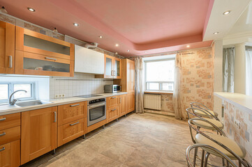well-lit kitchen with wooden cabinets, tile flooring, and a pink ceiling. There are stools at a counter in the foreground