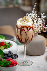 Elegant chocolate dessert drink. A tall glass of chocolate drink topped with cream sits on a table beside fresh fruit and a vibrant salad.