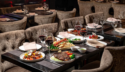 Elegant dining setup with gourmet dishes. A beautifully arranged table showcases gourmet meals, red wine, and elegant decor in a sophisticated restaurant.