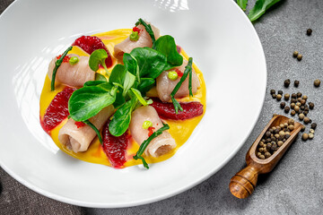 Elegant dish withunique style. This dish features rolled meat wrapped with greens on a vibrant sauce, garnished with fruits and herbs.