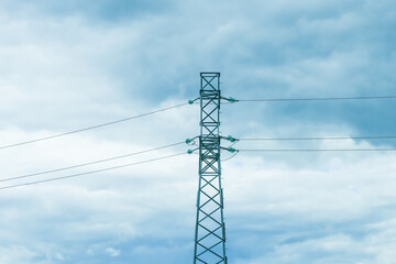 Obraz premium Electrical power line tower with wires against a cloudy blue sky. Electric transmission grid infrastructure for energy supply. Industrial landscape background.